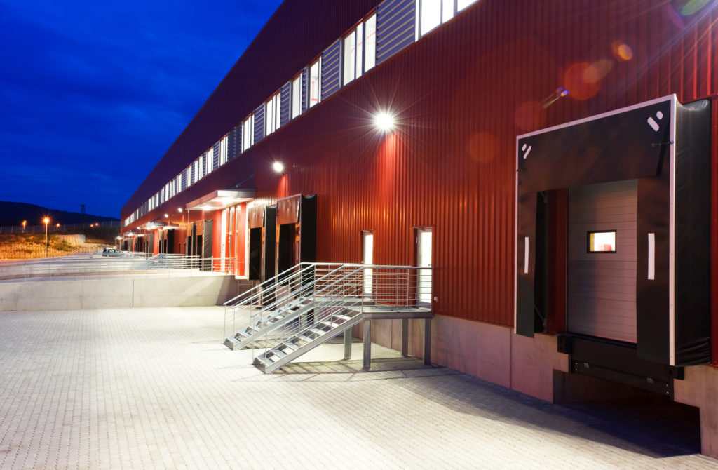Exterior view of a modern red warehouse building with loading docks at dusk.
